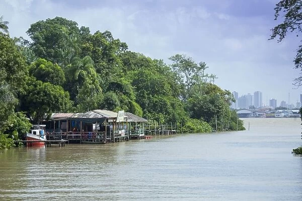 Boats and stilt house on an igarape (flooded creek) in the Brazilian Amazon with Belem city behind