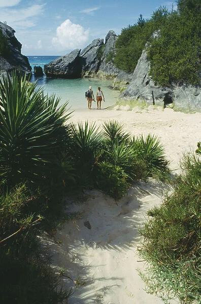 10025746. BERMUDA Jobsons Cove Couple at waters edge looking out to sea in secluded bay
