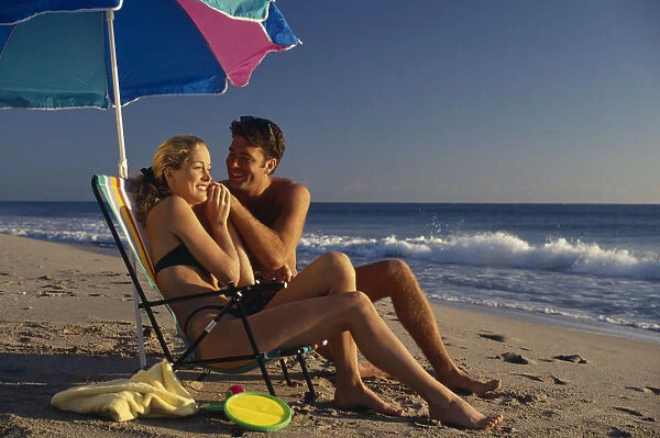 10027833. USA Florida Sunbathing Young couple on sandy beach sitting under a parasol
