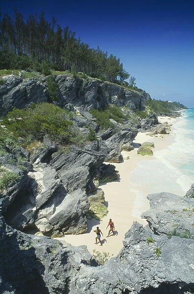 10032756. BERMUDA Astwood Park Couple walking on beach towards rocky cliffs