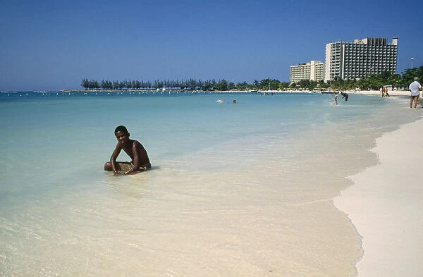10058137. WEST INDIES Jamaica Ocho Rios Sunbather on the beach with hotel behind