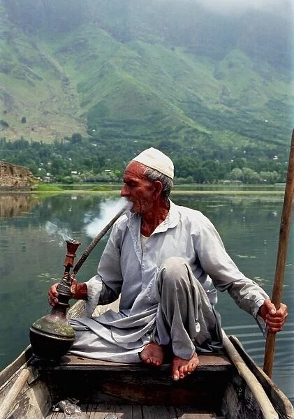 20046365. INDIA Kashmir Srinagar Nagin Lake. Man sitting in boat smoking a Hookah pipe