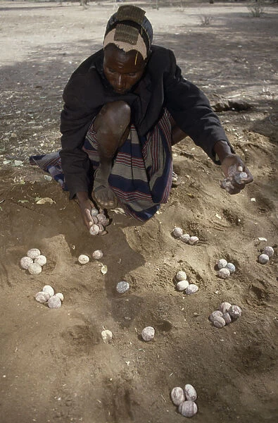 20053300. KENYA North People Turkana man playing traditional mathematical game of Ajua