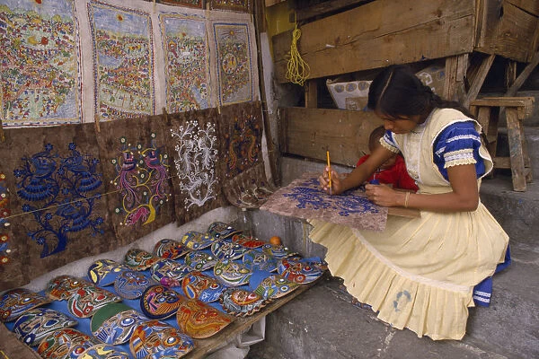20060837. MEXICO Puebla Taxco Young woman painting design on piece of bark with masks