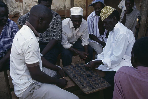 20075144. UGANDA Kampala Group of men playing board game of mweso in the street