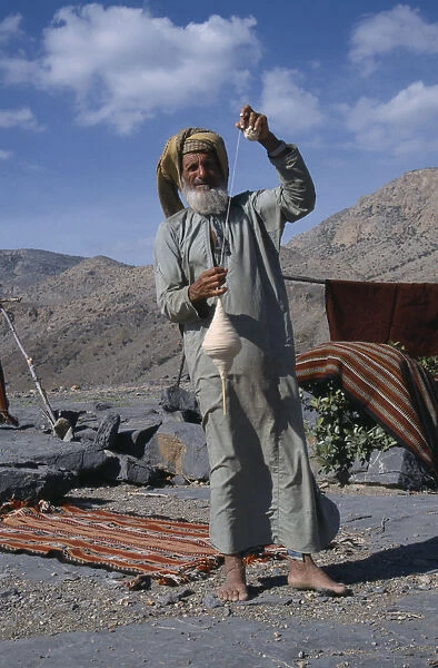 20086541. UAE Oman Jabal Shams Elderly man using spindle to spin thread for rug making