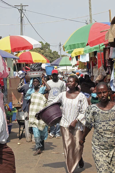 Bakau Market Atlantic Road. Busy market scene with crowds of people and roadside stalls beneath colourful striped sun umbrellas