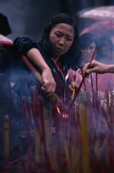 CHINA, Guangzhou Young woman lighting incense at temple