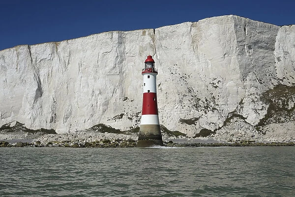 England, East Sussex, Beachy Head, Red and white painted lighthouse at base of cliffs