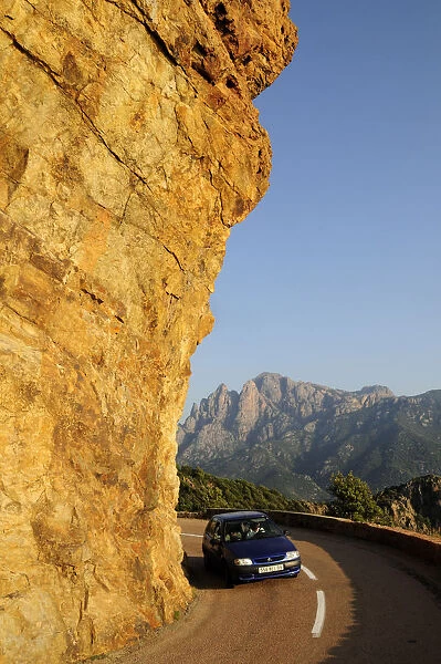 Golden rock face with coastal road & car near Porto