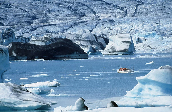 Iceland, Jokulsarlon Island, Distant boat on glacial lagoon with icebergs and glacial landscape