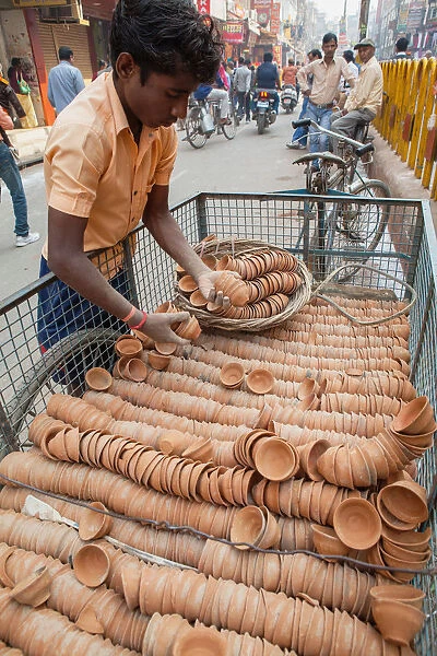 India, Uttar Pradesh, Varanasi, A deliveryman unloads clay cups, used to serve chai, from a bicycle trailer