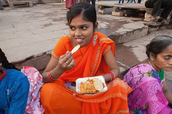 India, Uttar Pradesh, Varanasi, A woman eats a snack of bhel puri & kachori on the ghats