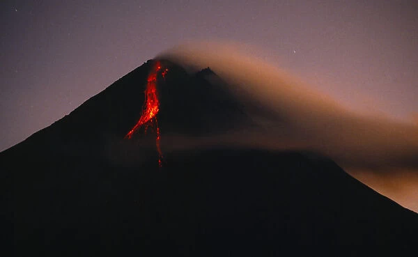 Indonesia, Java, Mount Merapi, Volcano erupting at dawn with lava flowing in a stream