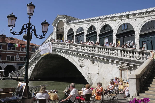 Italy, Veneto, Venice, Rialto bridge over the Grand Canal with cafe in foreground