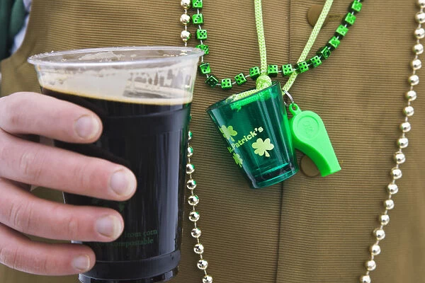 Detail of man wearing various green items whilst drinking pint of stout beer