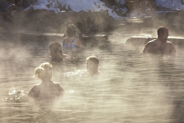 People in the outdoor hot pool of the spa resort with steam rising in the cold air