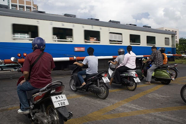 People on scooters at level crossing waiting train to pass