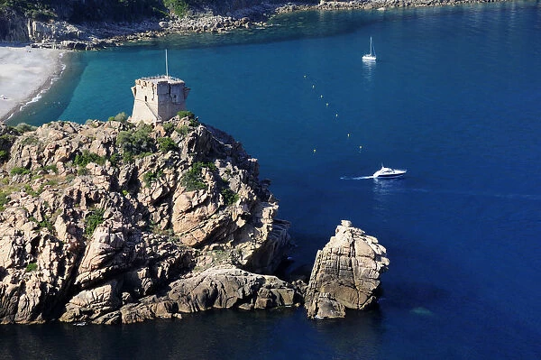 Porto Genoese tower on rocky headland with blue waters & boats
