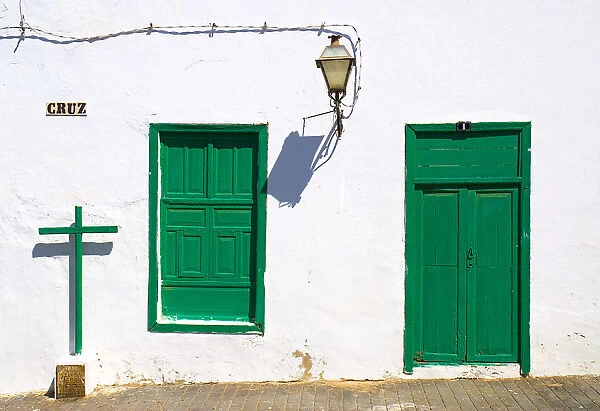 Teguise former capital of the island. Detail of house facade with typical white painted walls and green door and window shutters cross and lantern cast shadows