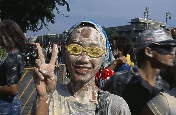 Thailand, Bangkok, Girl covered in mud wearing goggles with fingers held in the peace sign celebrating the Songkhran Festival. Thai New Year 15 April