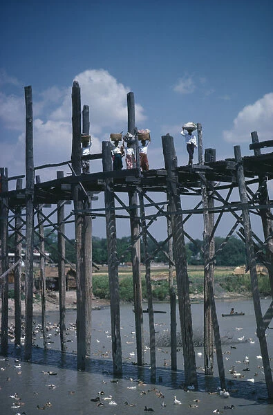 THAILAND Women carrying baskets on their heads crossing high wooden bridge across