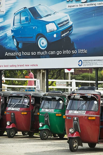 Tuk Tuks parked underneath advertising billboard for Suzuki WagonR