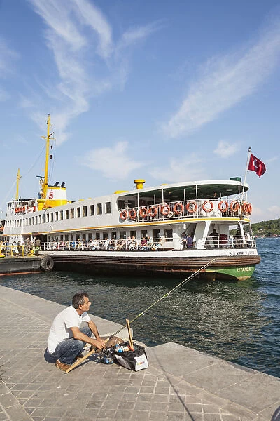 Turkey, Istanbul, Man fishing on quayside, and passenger ferry in Karakoy Cruise Terminal, Bosphorus Strait