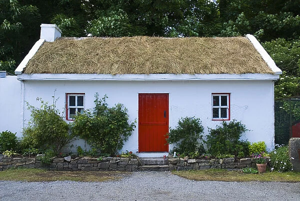 White painted cottage at Sligo Folk Park with red door and turf roof