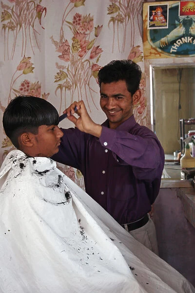 Young Indian barber in his barbershop cutting the hair of a boy