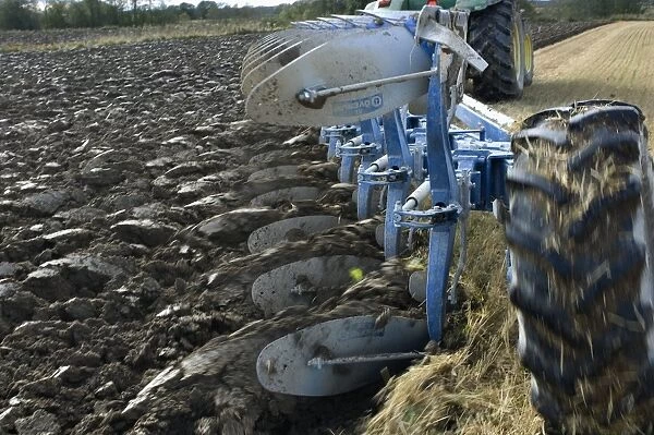 Close-up of eight furrow reversible plough pulled by tractor, ploughing stubble field, Sweden, autumn