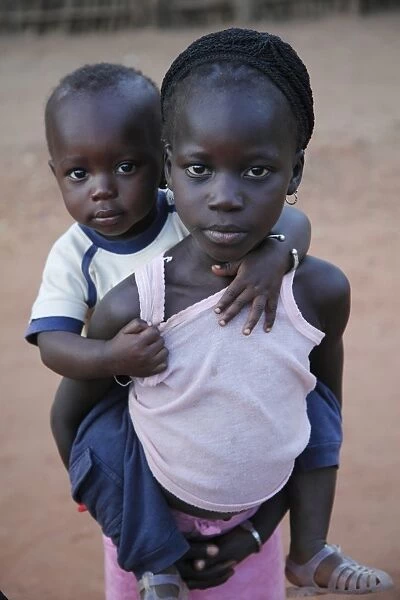 Young girl carrying younger brother on back, Gambia, january