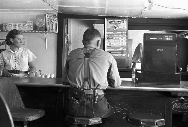 RESTAURANT COUNTER, 1939. A worker sitting at the food counter in a rural coffee shop in Alpine