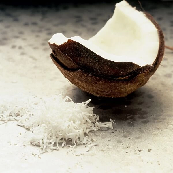 Broken coconut shell showing white meat, next to heap of grated coconut on kitchen worktop