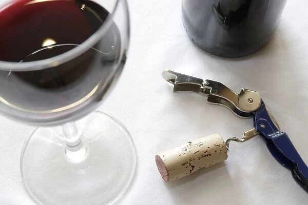 Corkscrew with cork next to glass of red wine