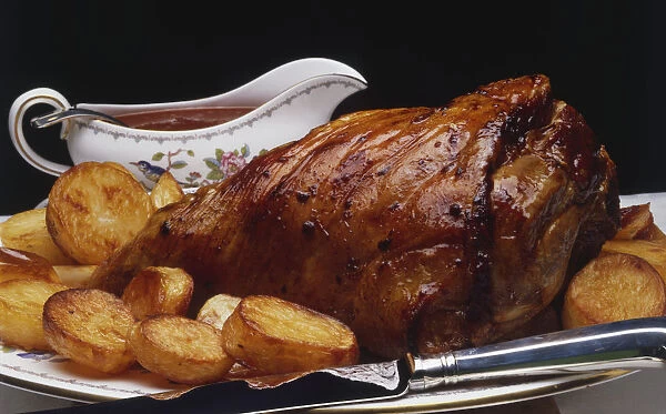 Roast pork served with roasted potatoes and a gravy boat, side view