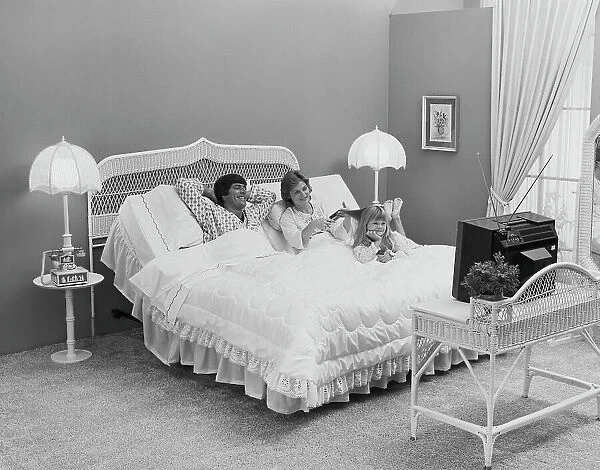 Father and mother with daughter lying on bed watching tv, smiling