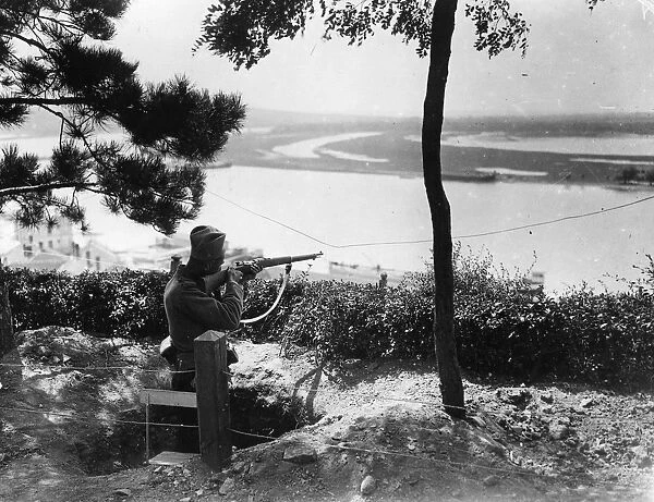 A Sniper. circa 1916: A sharpshooter aims over a river from high ground in Serbia
