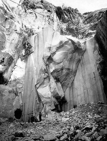 Excavators at work along a steep wall of a marble quarry in the Apuan Alps, Tuscany. (b  /  w photo)