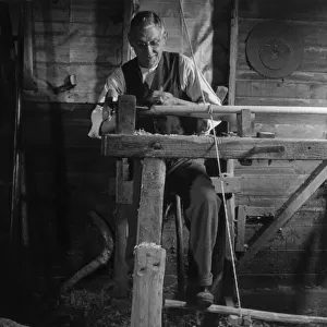 Turning wood on a pole lathe, which is turned by a foot pedal. Date: 1930s