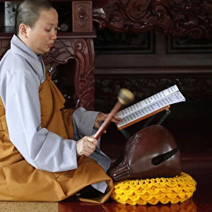 Buddhist ceremony at temple, monk playing on a wooden fish (percussion instrument)