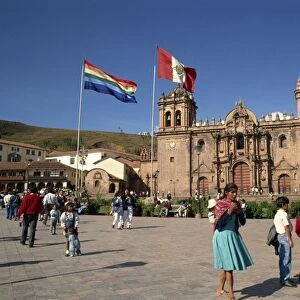 Groups of people and flags flying in front of the cathedral in Cuzco