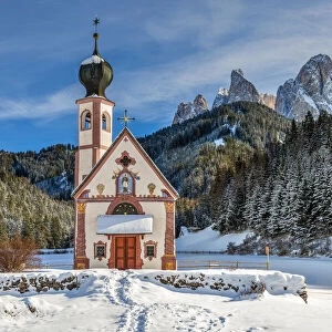 Scenic winter view over St Johann in Ranui church with Odle Dolomites behind