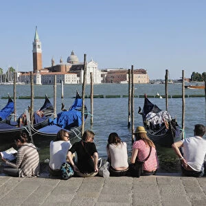 Italy, Veneto, Venice, gondolas & people sitting on waterside at Il Molo