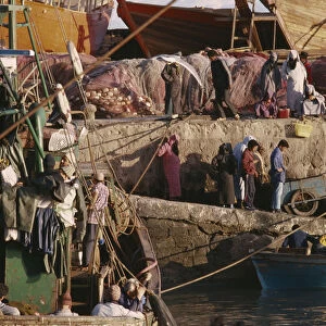 MOROCCO Essaouira Busy port scene with moored fishing boat and crowds on stone quay
