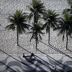 People sit on a bench on the sidewalk at Copacabana Beach in Rio de Janeiro, Brazil
