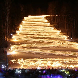 Spectators watch skiers descending down from the slope while holding lit torches in the