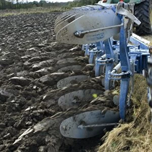 Close-up of eight furrow reversible plough pulled by tractor, ploughing stubble field, Sweden, autumn