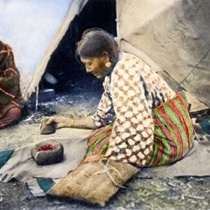 CHEYENNE WOMAN, 1890s. Using a stone mortar and pestle, a Cheyenne woman prepares wild cherries, pits and all, for the making of pemmican. Oil over a photograph, c1890s