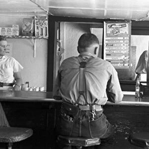 RESTAURANT COUNTER, 1939. A worker sitting at the food counter in a rural coffee shop in Alpine